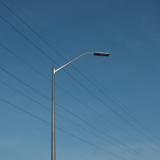 power lines and a lamppost, set against a blank blue sky. the power lines stretch diagonally from the top left to the bottom right of the frame.