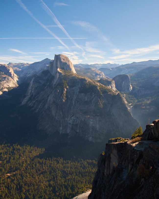 half dome and part of yosemite valley, viewed from Glacier Point and lit by the rising sun. half dome's face is in shadow, and the morning sun gives the trees in the valley a warm glow.
