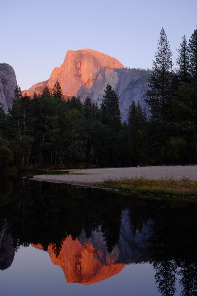 half dome lit by the setting sun, reflected by the merced river