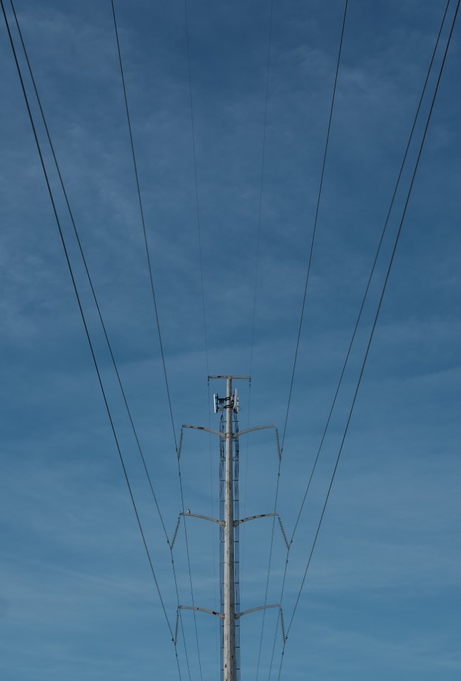 overhead power lines, suspended by a large tower. the image is taken from directly below the power lines, so they spread out symmetrically towards the top of the image.